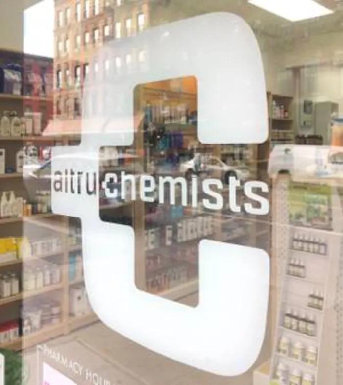 Altru Chemists logo decal on the pharmacy window with shelves behind